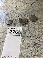 Three coins displayed on granite countertop: American half dollar, Canadian silver dollar, Canadian 50 cent coin all positioned alongside a MaxSold lot tag.