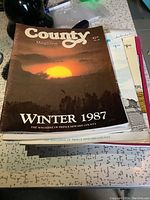 Stack of Prince Edward County magazines with Winter 1987 issue visible on top showing a sunset image on the cover