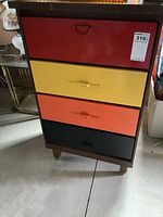 Front view of the dresser showing four drawers in red, yellow, orange, and black with varying handles and dark wood frame.