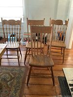 Four solid wood farmhouse chairs arranged in a row showing the overall set, finish, and condition including paint stains and wear.