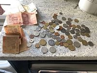 Two bags of assorted foreign currency coins and various denominations of paper bills photographed on a granite countertop.