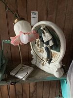 Front view of the metal and stone base lamp with frosted glass shade and the vintage chalkware figurine lamp on a wooden shelf.