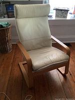 Front view of cream leather IKEA Poang chair with natural wood bent frame on wooden floor.