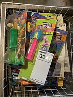 Photo showing assorted PEZ dispensers with various colored stems and character heads in packaging and loose in a white basket.