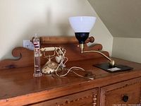 Overview of vintage phone, milk glass shade lamp, and water thermometer sitting on wooden surface.