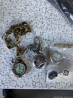 Lot items laid out include two pocket watches with chains, loose watch face, and small cross pendant.