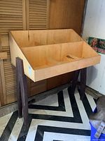 Full view of the record stand showing natural wood box with dividers and dark angled legs on a patterned floor.
