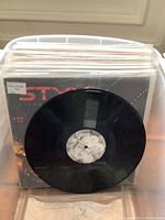 Overview of the vinyl records in plastic bin, showing Styx Kilroy Was Here album and one vinyl record out of its sleeve revealing label.