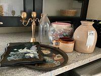 Overview of lot on countertop showing ceramic crock, glass milk jar, brass candelabra, wooden unicorn tray, ceramic mugs, and Coca Cola litho tray.