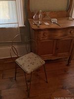 Vanity stool with metal frame and cream floral cushioned seat next to wooden vanity dresser with mirror.