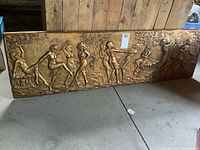 Full view of the elongated vintage chalkware wall art panel featuring multiple dancing figures in relief with a golden finish, showing overall wear and chips.