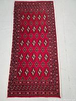 Full view of the Turkman wool rug showing the red background with geometric motifs and detailed border patterns.
