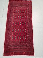 Full view of the rectangular Persian Turkman wool rug laid flat on a light surface, showing the intricate repeating geometric patterns primarily in red tones.