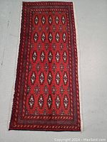 Full view of hand knotted Persian Turkman wool rug with repeating geometric patterns in vibrant red-orange and neutrals.