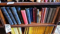 Shelf of antique books with four volumes of Blackie's Modern Encyclopedias in black leather and other old books including red and blue cloth covered volumes.