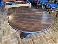 Front and side view of circular wood coffee table with dark wood finish and visible wood grain. Table has a round top and pedestal base. Shows some edge marks.