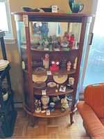 Front view of curved glass display cabinet showing four curved wooden shelves with various items inside, wood frame, caster wheels at base