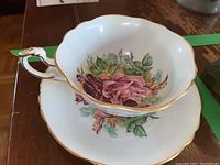 Close-up photo of the teacup resting inside the saucer. Visible detailed cabbage rose floral pattern and gold trim on the rims and teacup handle.