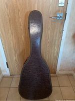 Brown molded hardshell acoustic guitar case closed against wooden door