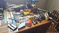 Wide top-view photo of all office supplies on wooden table including pens, stamps, calculators, stapler, tape holder, DVD-R discs, and chess set.