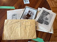 Five original 1830s engravings stored in protective sleeves, arranged on a wooden surface alongside an aged envelope inscribed with details.