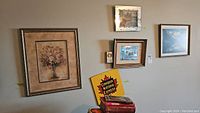 Five various framed prints on a wall including a floral print with an ornate gold frame, a Canadian National Express ad sign, a 3D moose travel art, and smaller moose print in wood frames.
