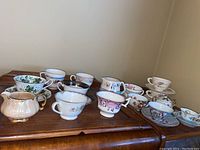 Photo showing a variety of twelve decorative teacups and saucers in assorted styles and colors on a wooden surface
