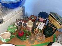 Photo showing various decorative tins, pottery salt and pepper shakers shaped like tomato and olive on a leaf tray, glass cream and sugar containers, and other vintage tins and small shakers.