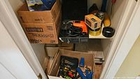 Photo of box with assorted hand tools including pliers, screwdrivers, and small hardware supplies