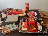 Overall view of assorted toys including red Signal Jr. wireless set, wooden maracas, Canada Post bank, Chiclets dispenser with elf head, toys in original boxes and vintage game pieces on black table