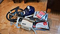 Photo showing Electrolux Ergospace vacuum and Hoover vacuum, hoses, tubes, floor heads, filters, and bags on floor.