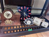 Wide shot showing all vintage clocks including the wooden mantel clock with horse sculpture, the Las Vegas domino clock, crystal glass clock, and four white electric alarm clocks.