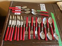 Full set of cutlery arranged in rows showing knives, forks, soup spoons, and teaspoons with red handles.