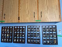 Four wooden spice racks with 12 glass spice bottles arranged and mounted on a wall under kitchen cabinets.