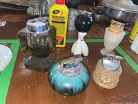 All five vintage table lighters shown together with a yellow bottle of Ronsonol lighter fluid on a wooden table.