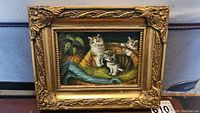 Full view of framed miniature cat painting showing three kittens inside a basket with fabric and greenery
