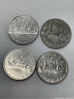 Reverse sides of four large Canadian one dollar coins showing the canoe designs and years 1975, 1980, 1981, 1986.