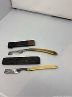 Two antique foldable straight razors with protective sleeves shown on a white surface.