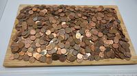 Wide shot showing a large quantity of mixed pennies spread out on a wooden surface.
