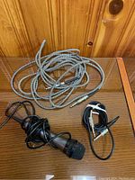 Photo displaying two male-to-male cables including a braided high-grade cable and a smaller black cable, plus a wired black microphone on a wooden surface.