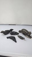 Wide view of all five Inuit stone carvings on white background, showing different animal figures including a seal, whale, bird, turtle, and otter-like animal