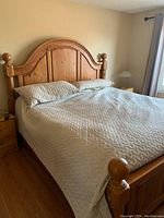 Full view of king size bed frame with beige quilted bedding, showing wood headboard with curved top and ball finials.