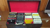 Open black textured storage case displaying rows of vintage 8-track music tapes inside red felt lining