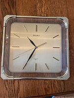 Full view of Seiko square wall clock placed on wooden surface showing design and condition