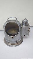 Front and side view showing metal binnacle body, glass window for the compass dial, and attached lamp housing with hinged door.
