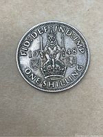 Reverse side of the 1948 George VI one shilling silver coin depicting a crowned lion standing on a crown, year, denomination, and additional inscriptions.