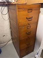 Full view of the vertical filing cabinet showing four drawers with metal handles and label holders, solid wood construction with paneled sides.