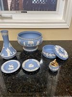 Full view of six-piece Wedgwood blue jasperware collection displayed on table beneath window.