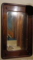 Full view of the antique wood framed mirror reflecting a wooden wall and part of a staircase.