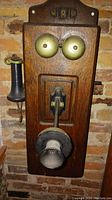 Front view of telephone mounted on brick wall showing oak backplate, brass bells and mouthpiece